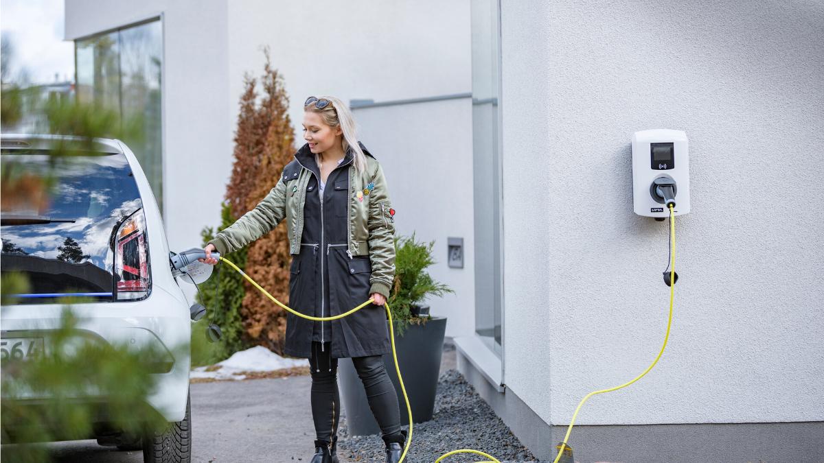 Nainen lataa sähköautoa