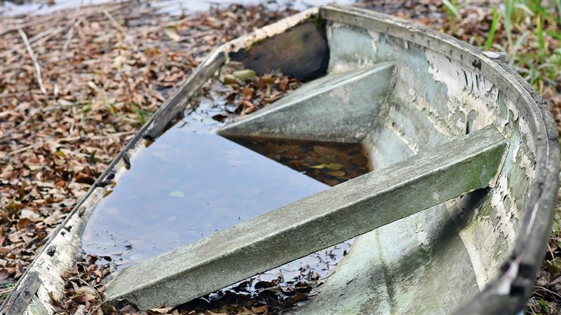 Huonokuntoinen veden täyttämä lasikuituvene rannalla. Kuva: Vastavalo
