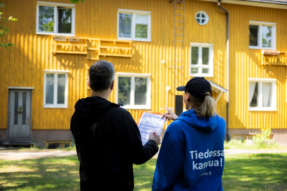 Kuvituskuvassa mies ja nainen katselevat paperia keltaisen puutalon edessä.